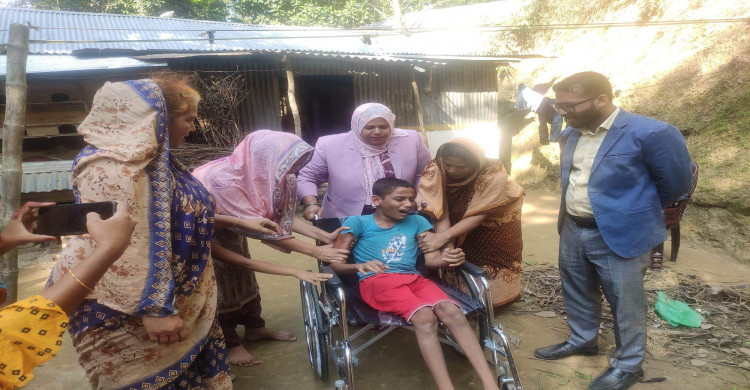 প্রতিবন্ধী রিফাতকে হুইল চেয়ার তুলে দিচ্ছেন কাপ্তাই ইউএনও।